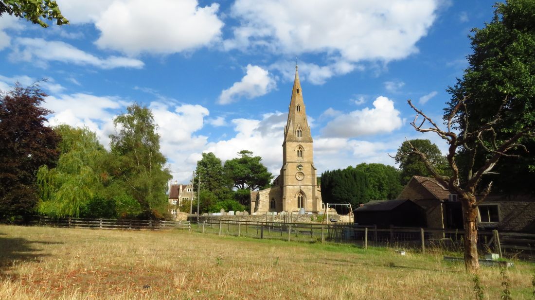 St Peter's Church, Aldwincle: a 14th-century broach spire rises from a square limestone west tower above the village churchyard, seen across rough grazing land in summer