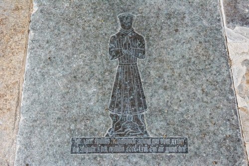 The memorial brass of William de Aldwyncle, 1463, set in the chancel floor of All Saints' Church: a standing figure in a long gown, hands clasped in prayer, with a dog at his feet and a Latin inscription beneath